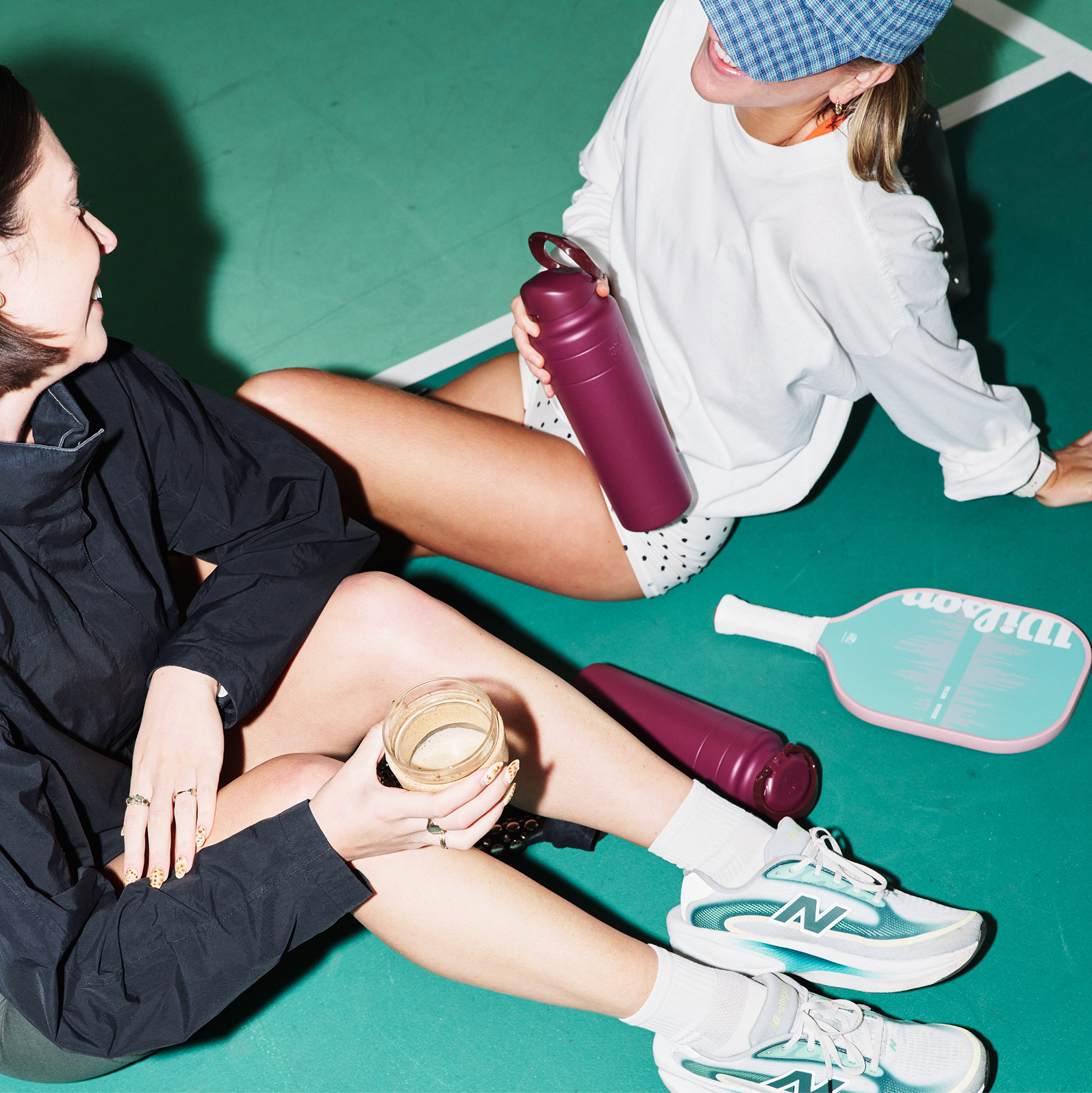 Two girls sitting on a pickleball court talking with two Mulberry Ora Water Bottles