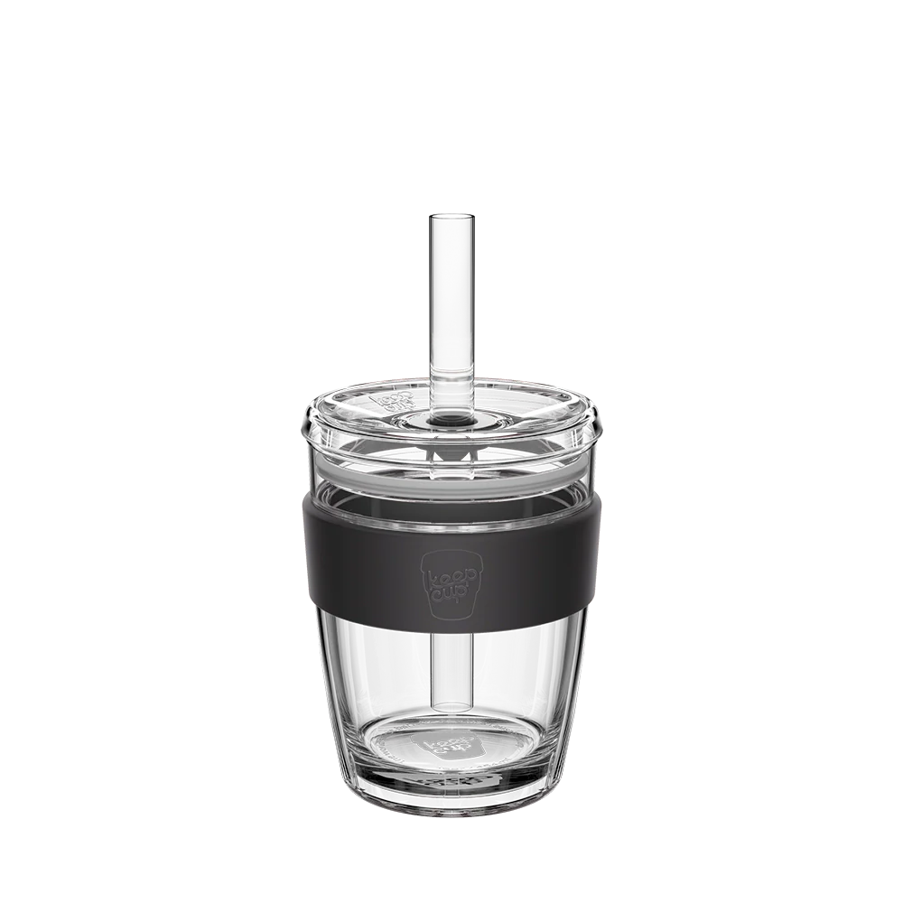 Clear glass tumbler with black sleeve and straw on a white background