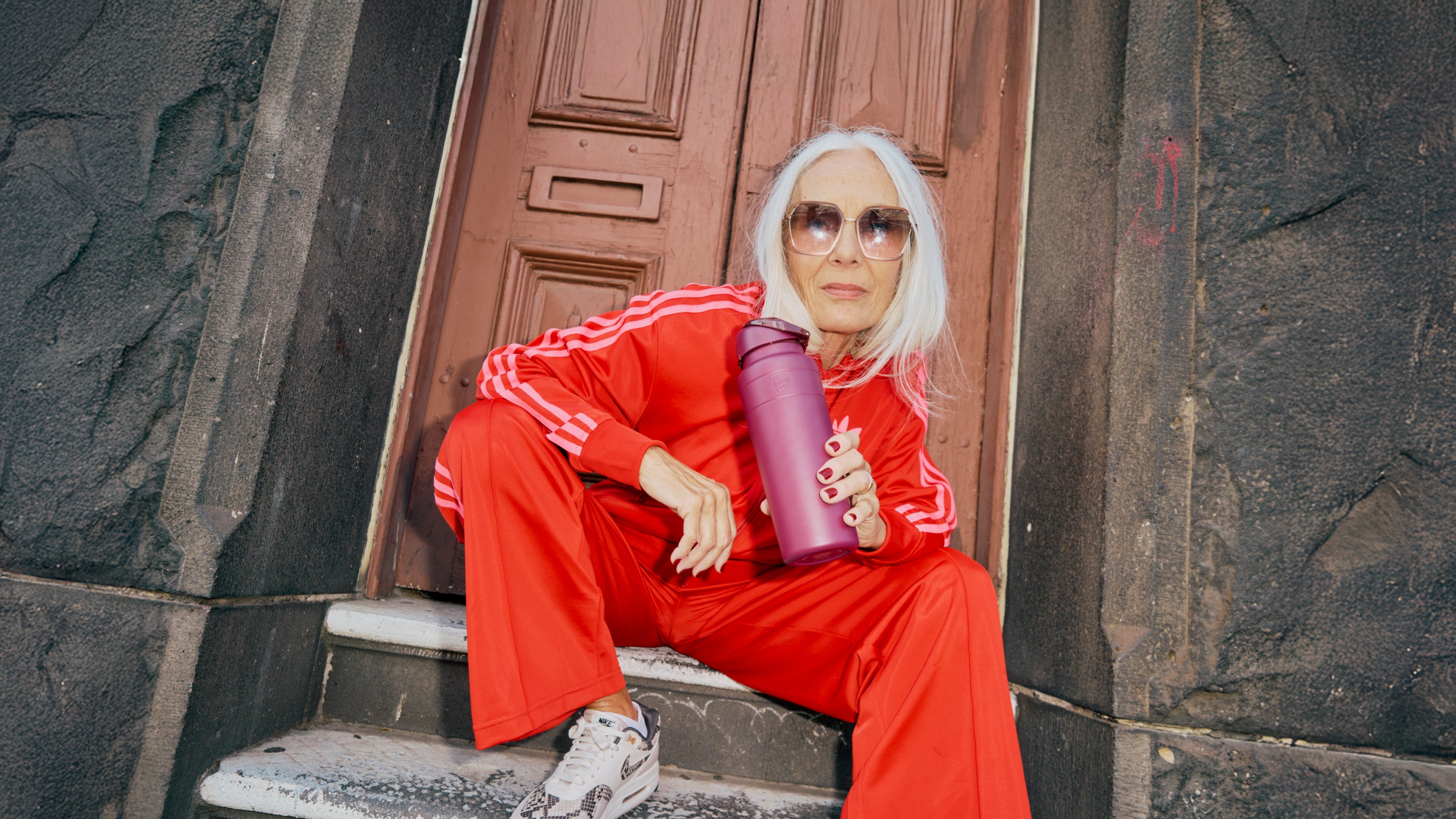 Person in red tracksuit holding a mulberry water bottle sitting on steps.
