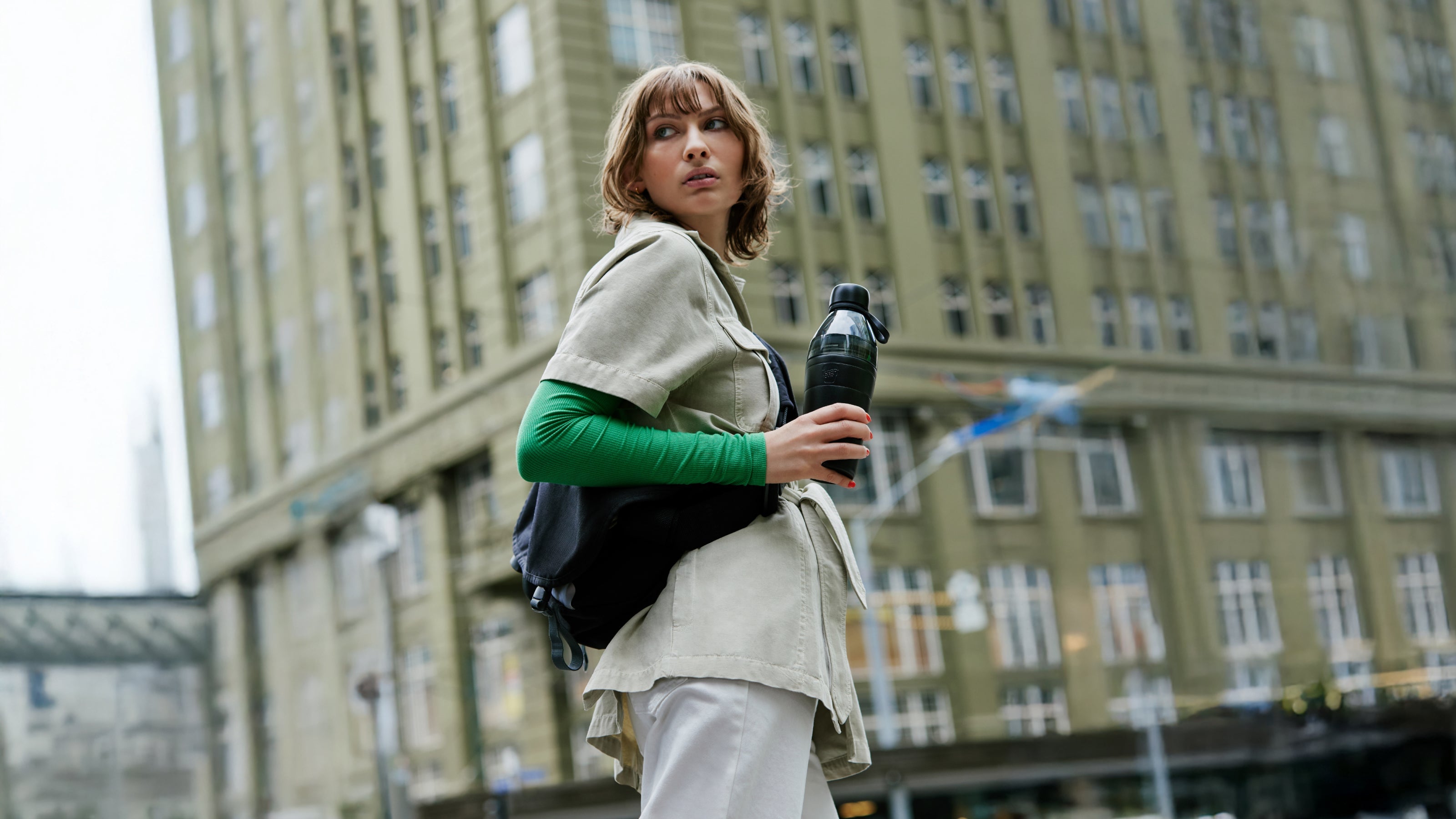 Woman holding a water bottle in an urban setting with a blurred building in the background