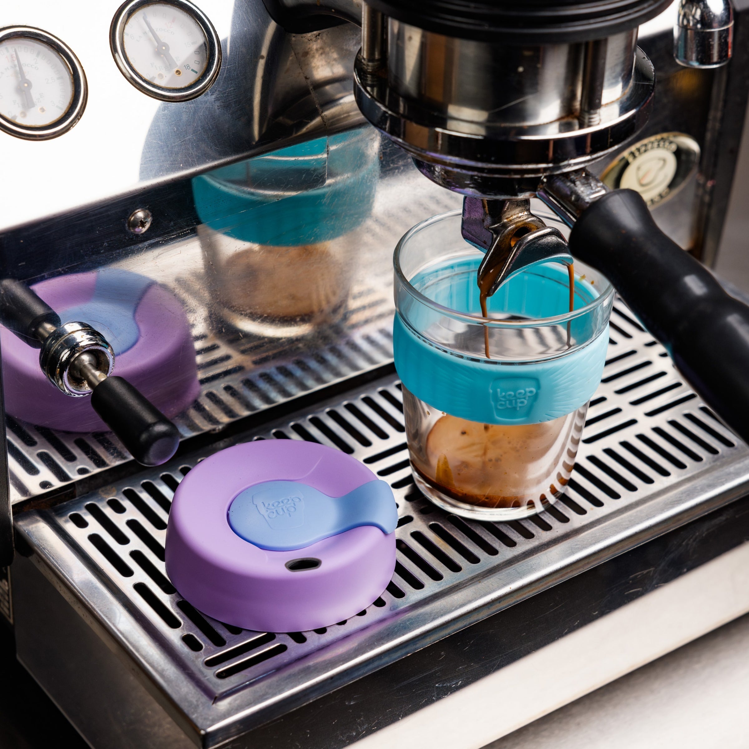 Espresso machine with glass cups and colorful silicone sleeves on a metal surface.