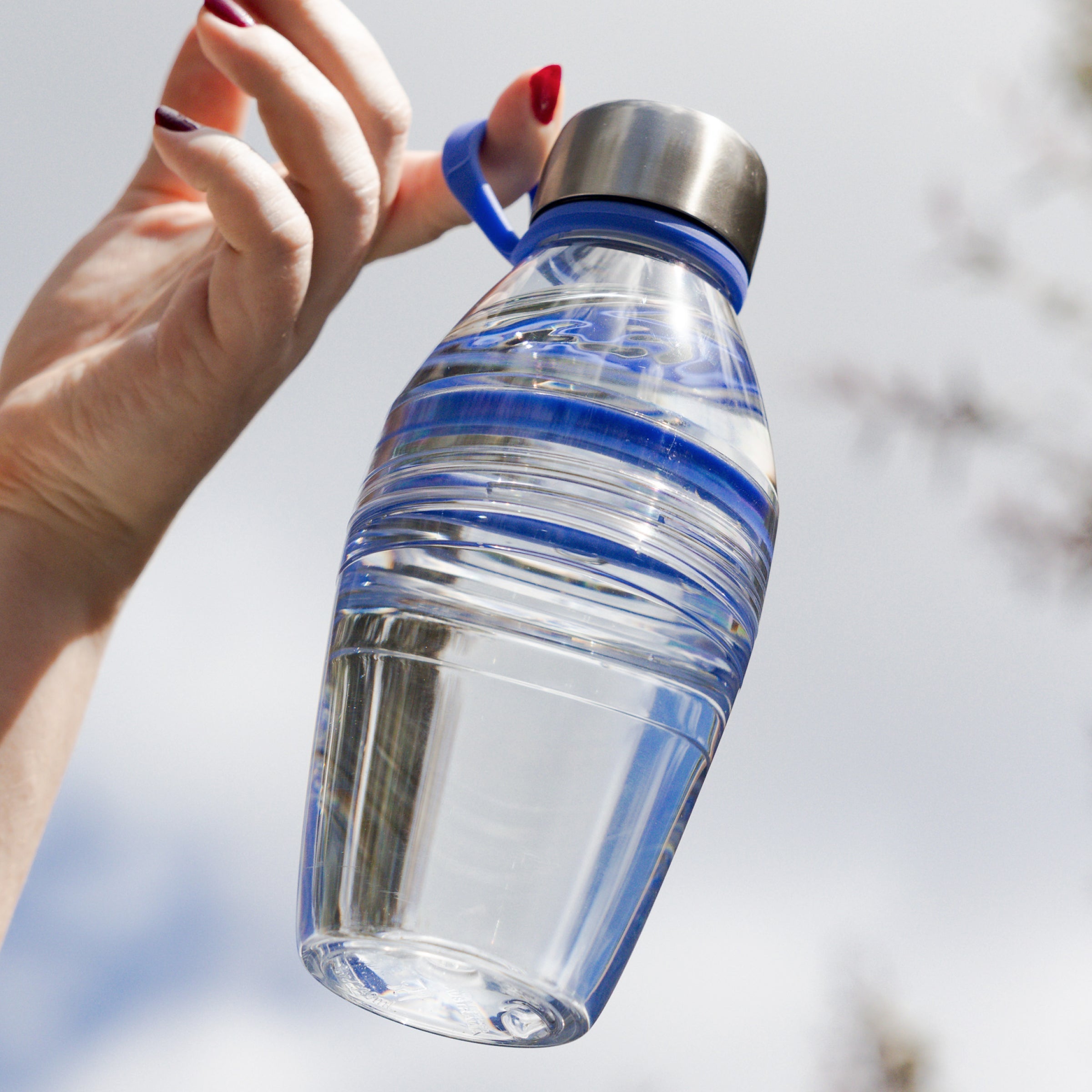 Clear water bottle with blue accents held by a hand against a blurred natural background