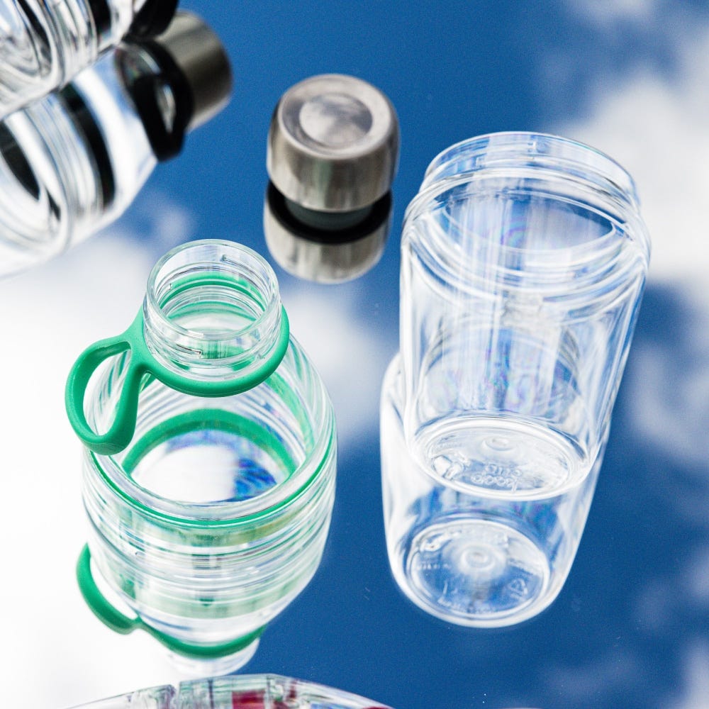Clear water bottles with green cap and silver cap on a reflective surface