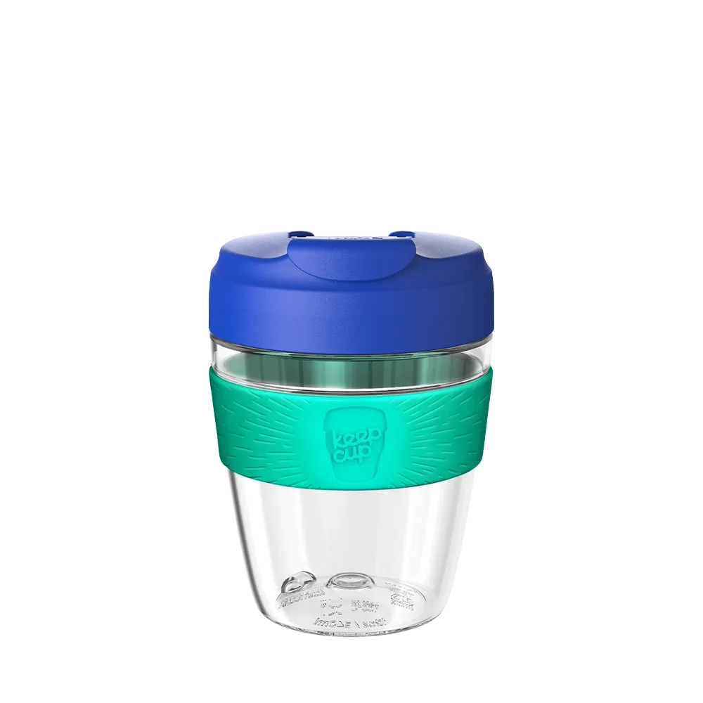 Clear reusable coffee cup with blue lid and green sleeve on a white background
