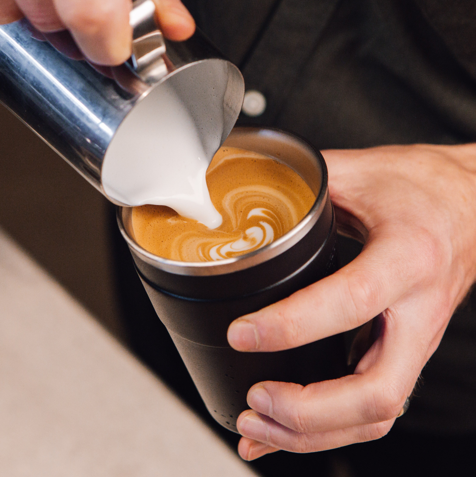 Person pouring milk into a coffee cup with latte art