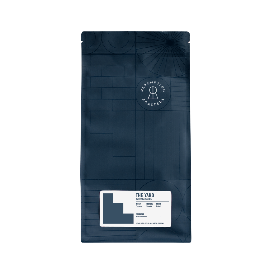A dark navy blue 1 kg coffee bag from Redemption Roasters featuring The Yard blend, with geometric patterns on the packaging and a white label showing tasting notes of red apple and caramel.