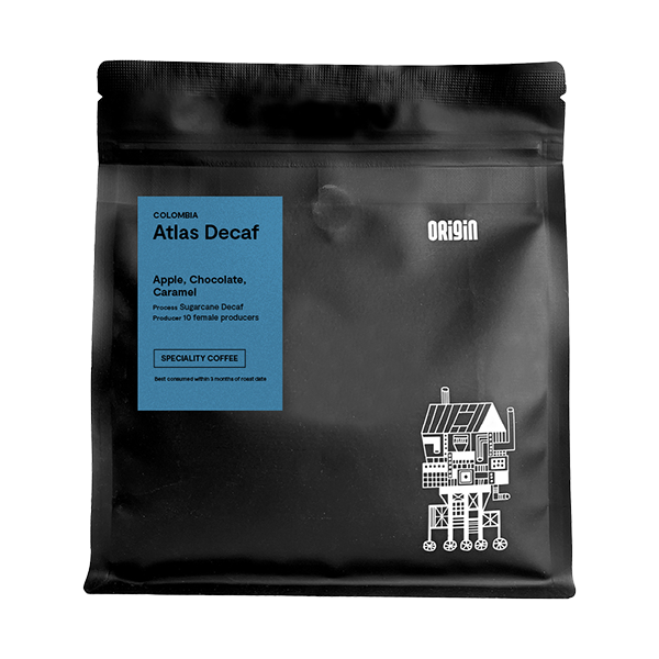 Black matte coffee bag for Origin Colombia Atlas Decaf 250g, featuring a blue label with tasting notes of apple, chocolate and caramel, and a white illustrated design of stacked houses on the lower right corner.
