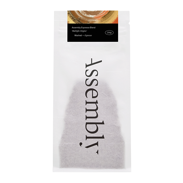 A 200g bag of Assembly Espresso Blend coffee in white packaging with the brand name printed vertically in grey text, featuring a label showing "Multiple Origins" and "Washed — Espresso" details against a golden swirl design at the top.