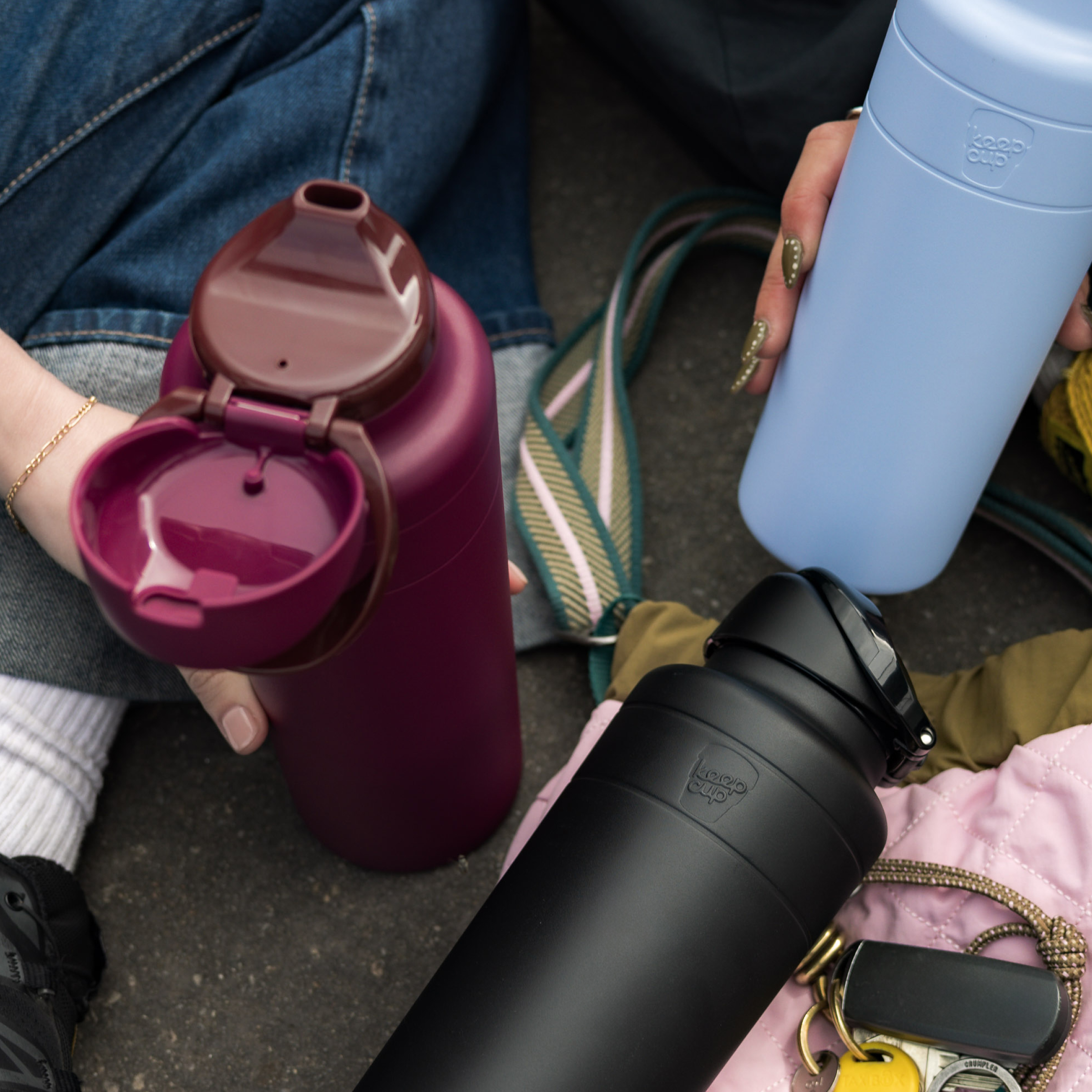 Three insulated water bottles held by people on a street.