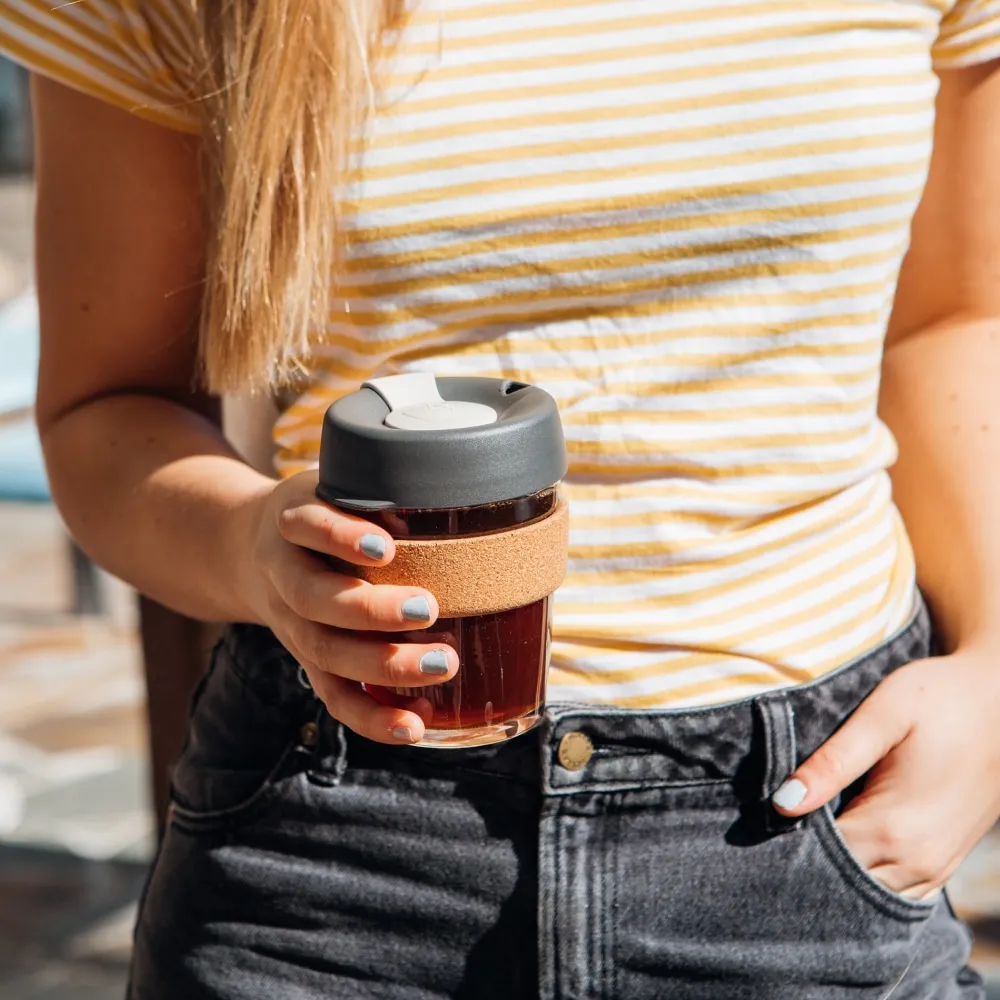 Person holding a reusable glass coffee cup with a scenic background
