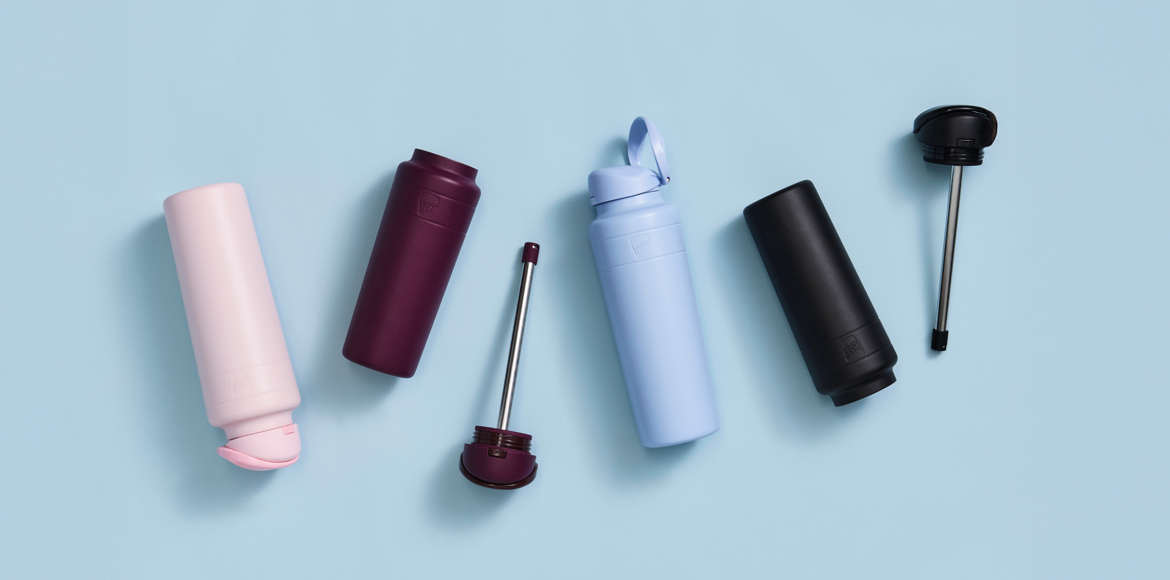 Collection of Ora Bottles on a light blue background with the lid separated, showing the metal straw and removable silicone flow control valve.