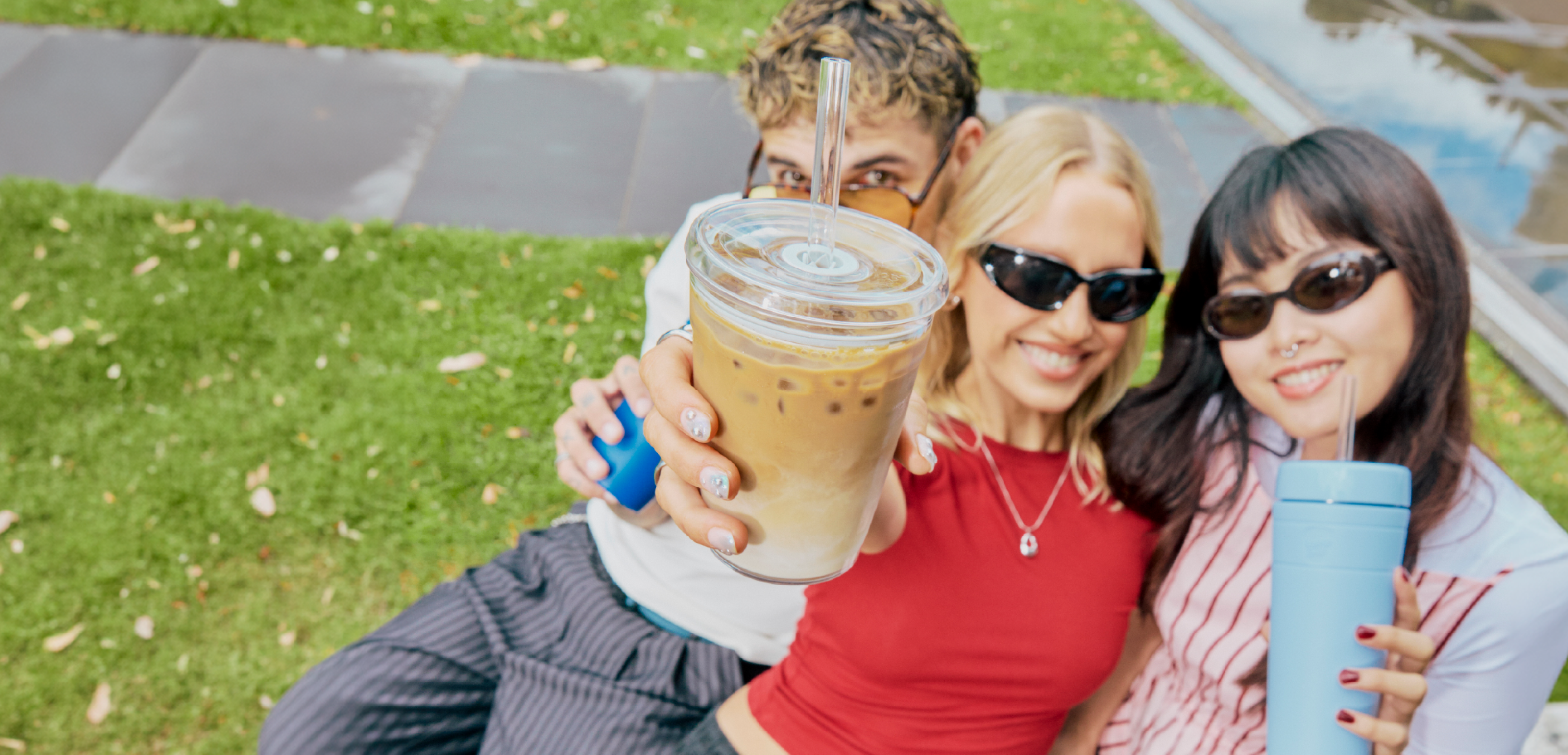Three people sitting outdoors holding an Original Cold Cup with iced coffeen inside and another person holding a Commuter Cold Cup in Orchid.