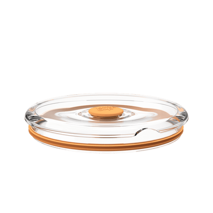 Go Bowl Flat Lid in Peach, shown from a low side angle against a white background, featuring a clear plastic lid with an orange silicone rim and central press-button seal.