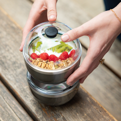 Person holding a container with granola and fruit on a wooden surface