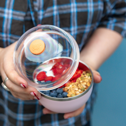 Person holding a container with a lid open, revealing berries and granola.