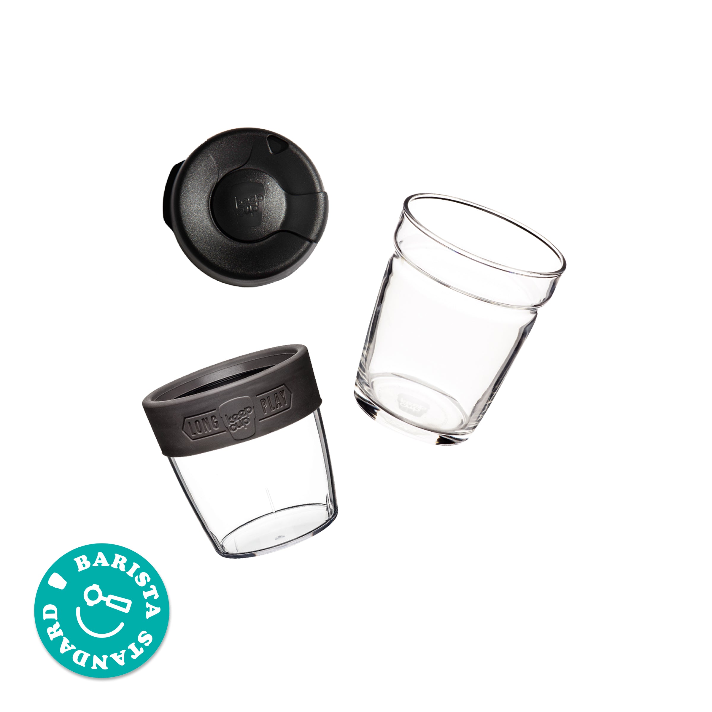 KeepCup Brew Longplay M 12oz shown as an exploded view with components separated: splashproof lid, clear glass cup, clear plastic outer sleeve with black silicone band marked "Long Play", and an additional clear glass cup, accompanied by a circular sticker reading "Barista Standard".