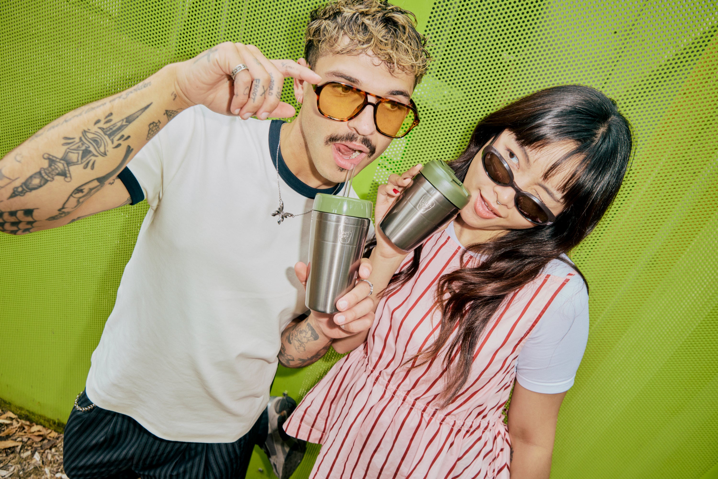 Two people drinking from stainless steel water bottles with green lids against vibrant green background