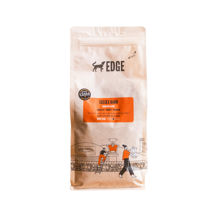 A 1 kg bag of Sussex Barn Signature Blend coffee from Edge, featuring a cream-coloured stand-up pouch with an orange label describing chocolate, berries and marzipan tasting notes, illustrated with a scene of people at a coffee roastery and displaying a Great Taste award badge.