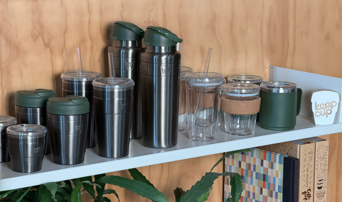 The Nitro Pine retail range including, Brew Cork, Commuter travel cup, Cold Cup Origjnal, Ora insulated water bottle, Commuter insulated Cold Cup, Cold Cup longplay and Go Bowl Luxe, on a white shelf against a wood-paneled wall.